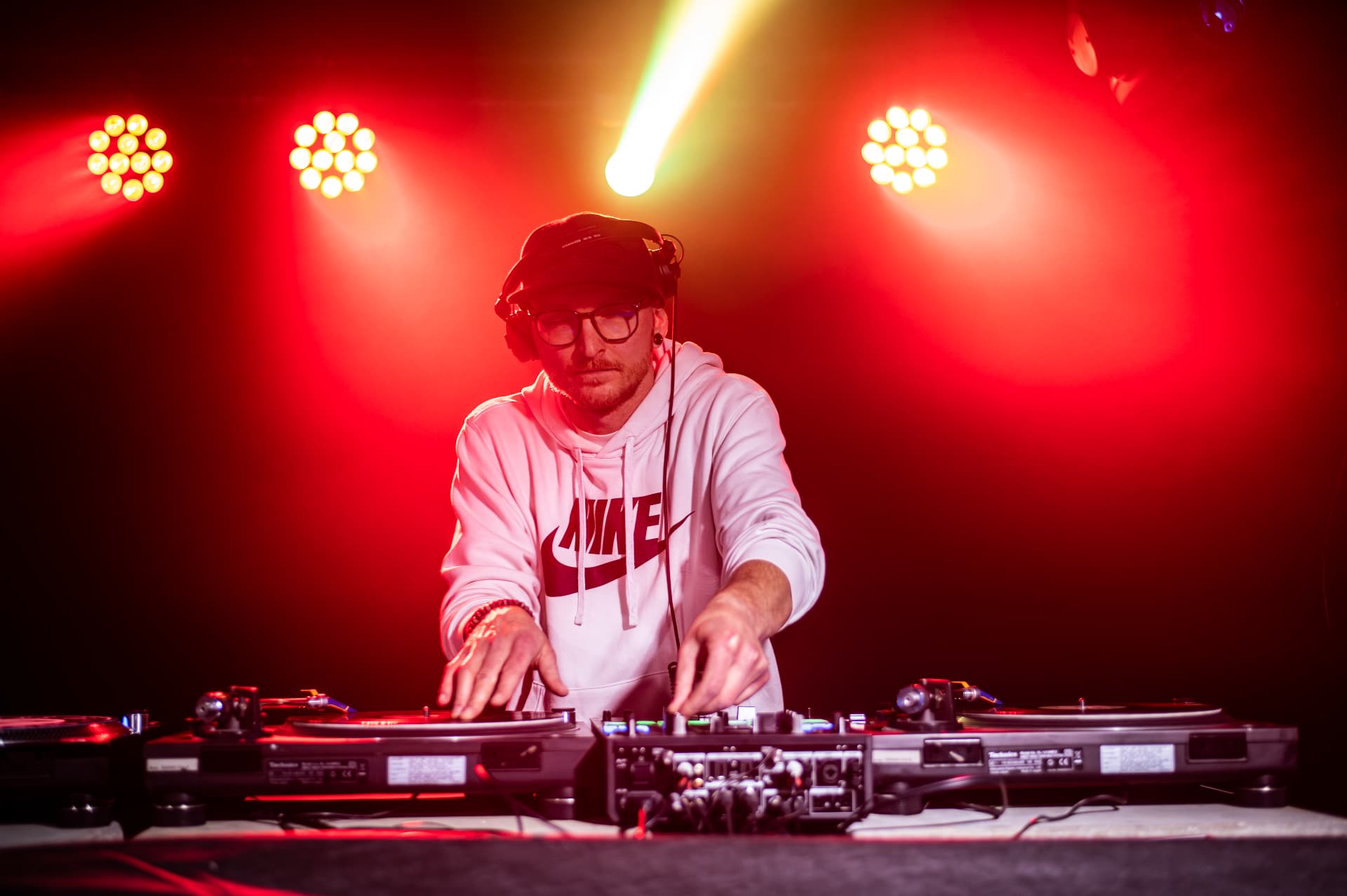 DJ v bílé mikině za gramofony v červeném světle